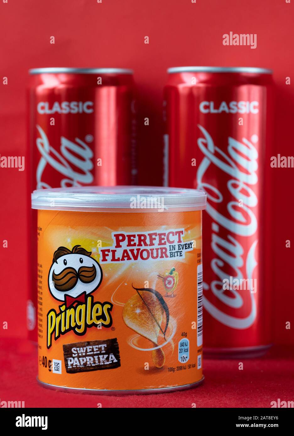 Röhre aus Pringles Chips und zwei Dosen Coca-Cola auf rotem Hintergrund Stockfoto