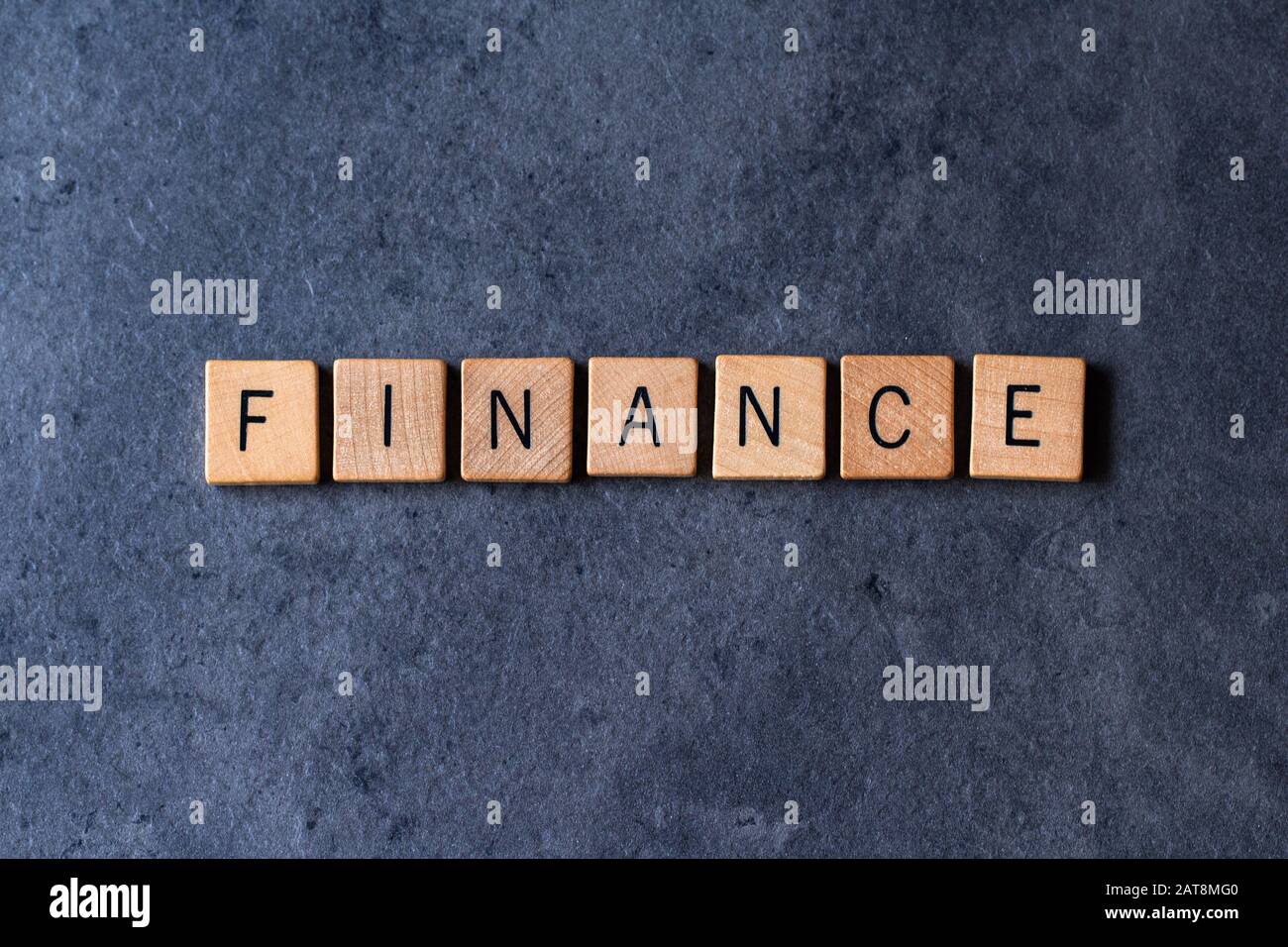 "Finance" buchstabierte in Holzbrieffliesen auf einem dunklen, rauen Hintergrund Stockfoto