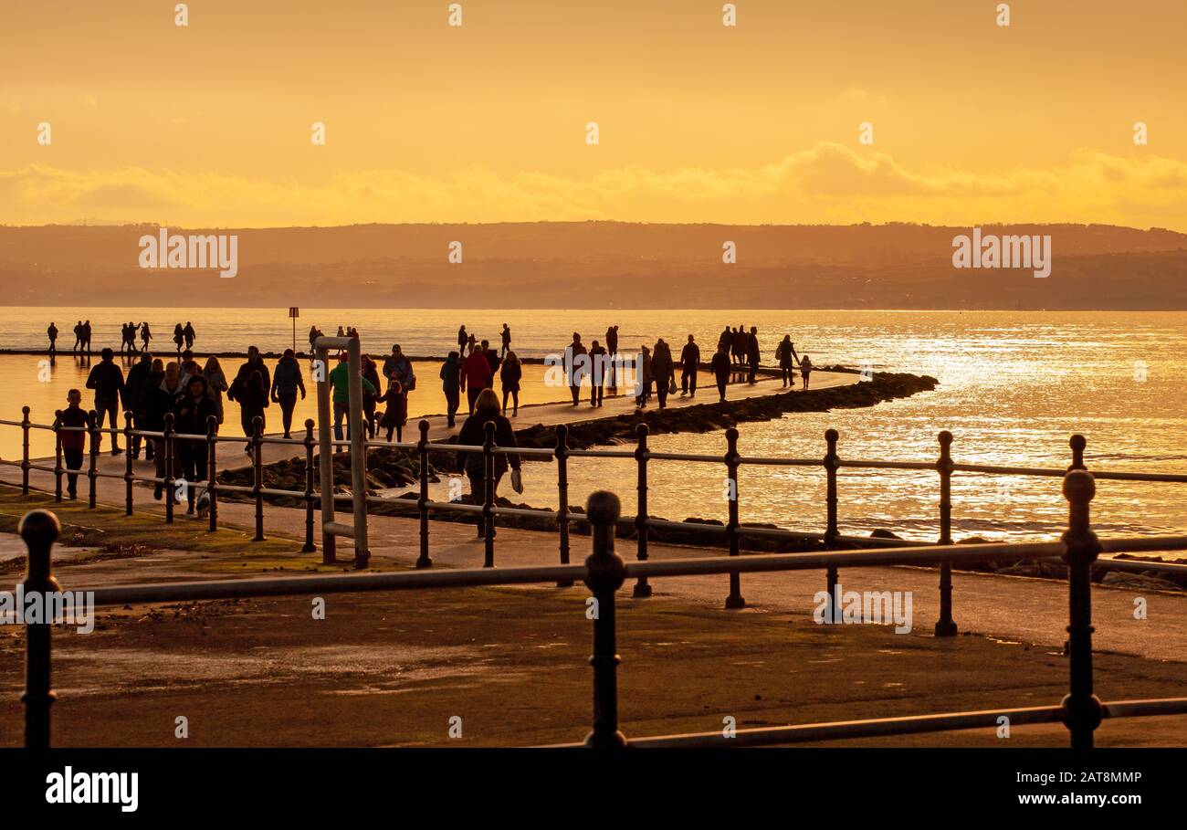 Menschen, die auf der Wirral-Halbinsel bei West Kirby auf dem Meeressee spazieren, untergehen bei Sonne auf dem Wandpfad zwischen Bootssee und der Dee-Flussmünde Stockfoto