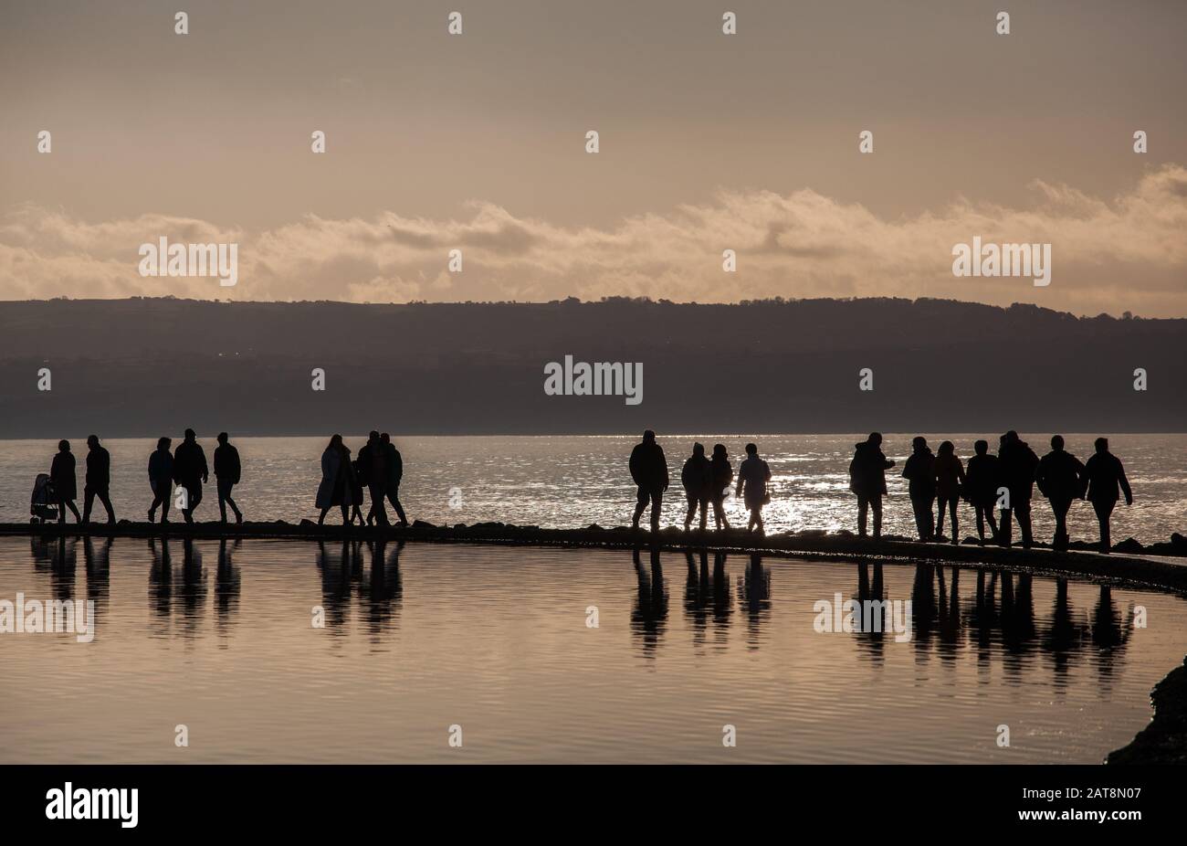 Menschen, die auf der Wirral-Halbinsel bei West Kirby auf dem Meeressee spazieren, untergehen bei Sonne auf dem Wandpfad zwischen Bootssee und der Dee-Flussmünde Stockfoto