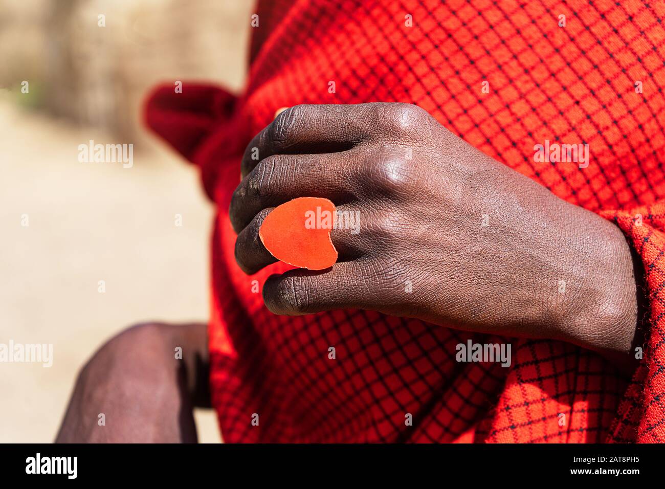 Afrikanischer Mann, der einen schwelenden Kuchen mit einem roten Herzring in den Händen hält. Tansania, Afrika. Stockfoto