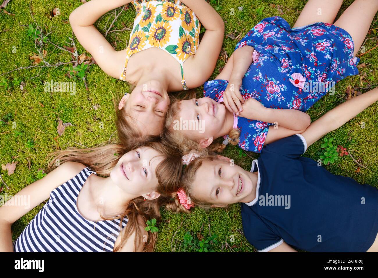 Mädchen verschiedener Altersgruppen, die in einem Sommerwald zusammen auf einem Moos liegen und die Sommerferien im Freien genießen Stockfoto