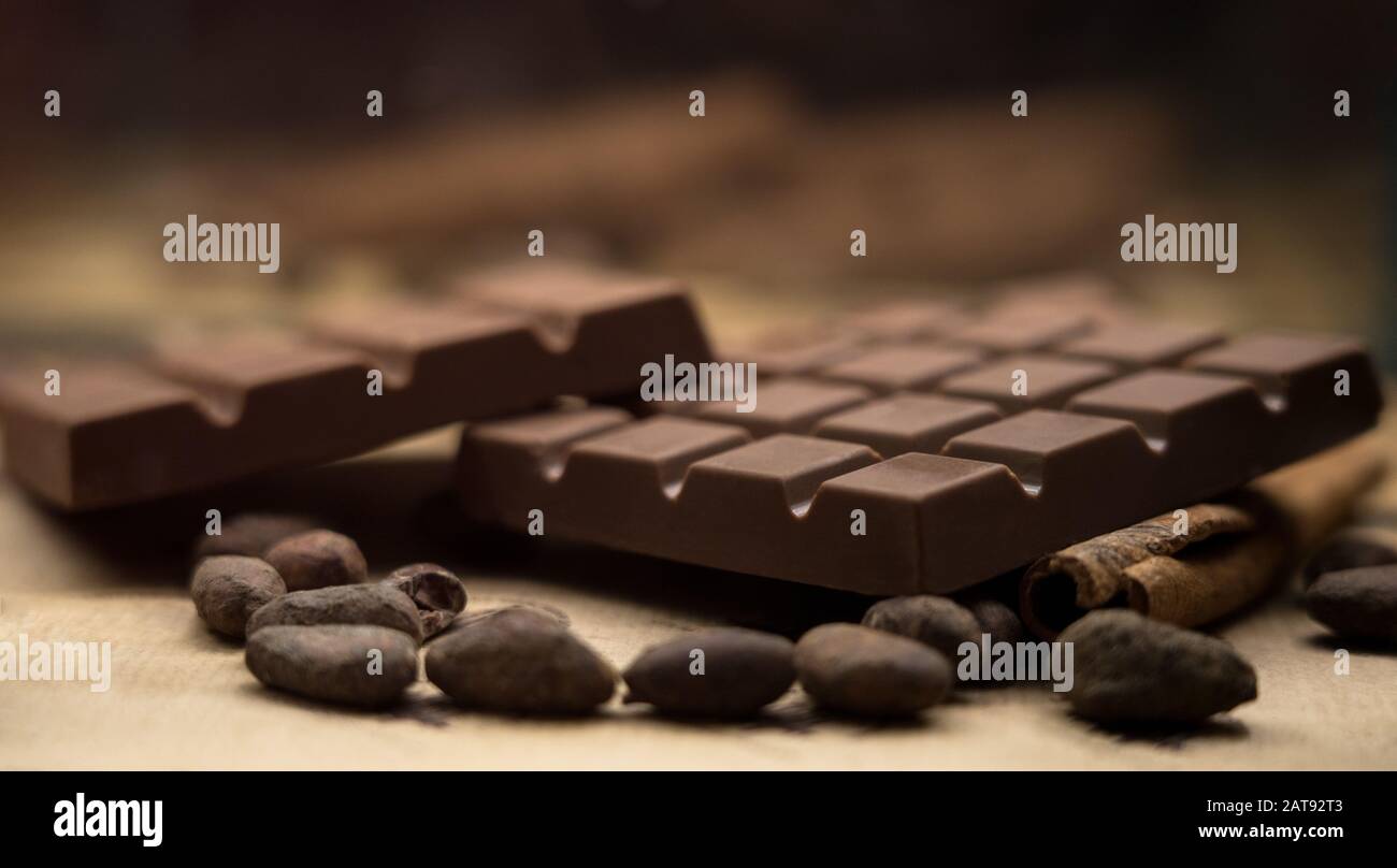 Braune Schokoladenriegel und Kakaobohnen und Zimtstab auf dem Tisch mit verschwommem Hintergrund Stockfoto