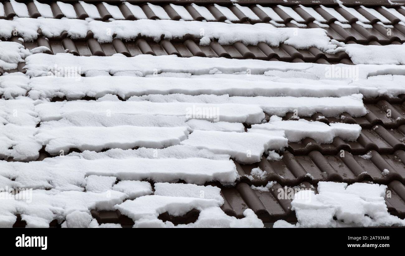 Auf den Dachziegeln taut Schnee. Malerischer Winterwetterhintergrund. Ein schneebedecktes Dach, auf das eine Dachlawine abging. Stockfoto