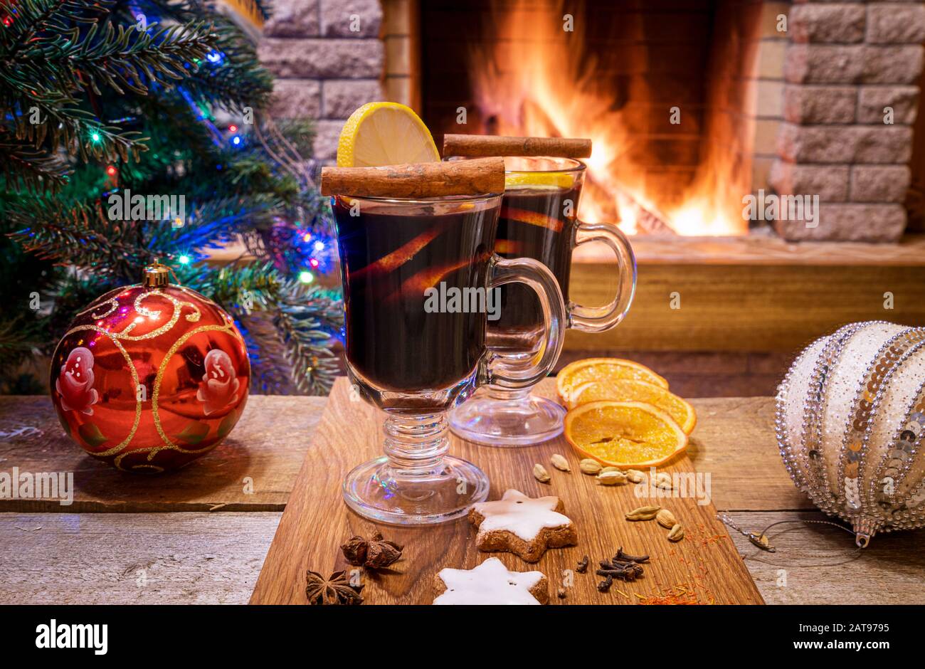 Gemütliche Weihnachts-Szene mit zwei Gläsern Glühwein auf einem Holzbrett vor dem brennenden Kamin. Stockfoto