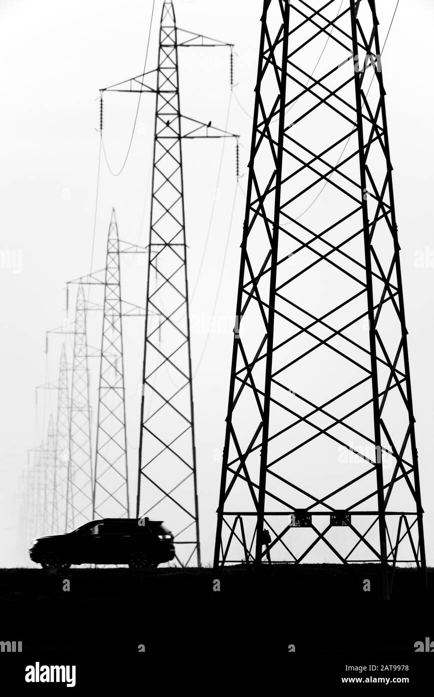 Auto in der Nähe von Leitungen für die allgemeine Übertragung von elektrischer Energie in einer nebligen Landschaft Stockfoto