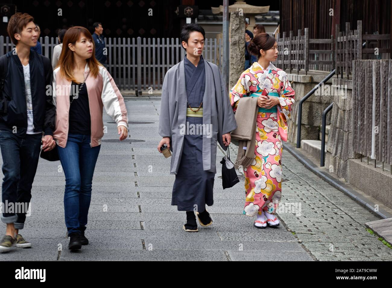 Zwei junge Teenager (Mann und Frau) trugen einen Kimono auf der Straße in Kyoto, in der Nähe eines jungen Paares, das sich im modernen westlichen Stil kleidete. Stockfoto