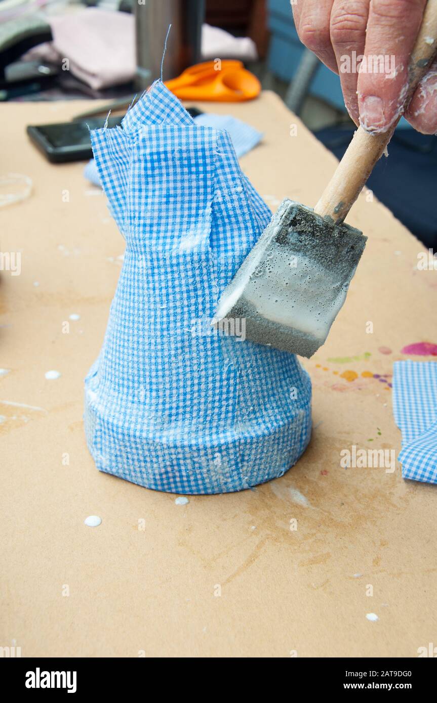 Handwerk Projekt Stoff Blumentopf mit einer Hand malen ein Kunsthandwerk über dem blauen Gingham Stoff auf dem Ton Blume Topf machen hausgemachte Handwerk. Stockfoto