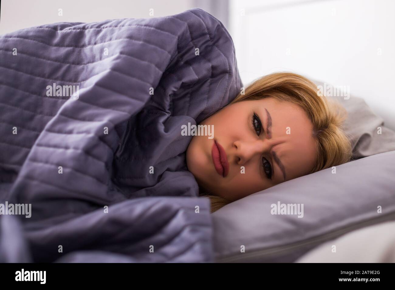 Erschöpfte Frau, die Fieber hat und in ihrem Bett liegt, alle in Federdecke eingewickelt. Stockfoto