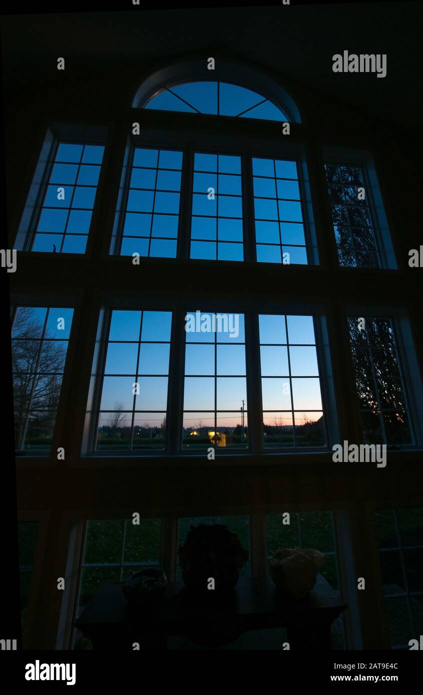 Großes Fenster bei Sonnenuntergang mit dramatischer Beleuchtung. Senkrecht hohe Innenfenster mit einem halben Kreis oben am Abend fallen. Stockfoto