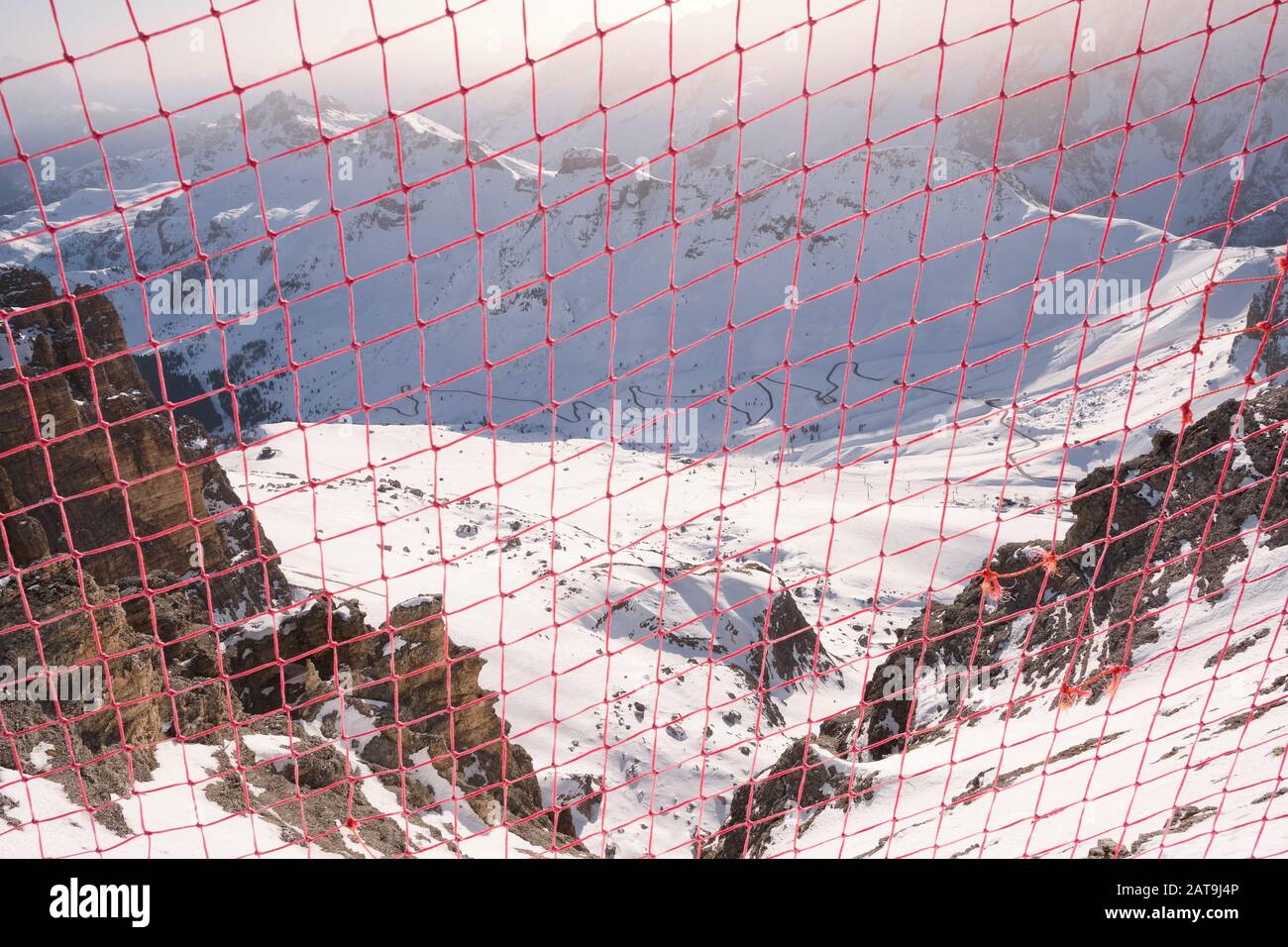 Sicherheitsnetz am Rande eines Bergrückens im Winter mit Blick auf den Pass Pordoi unterhalb und die kurvenreiche Straße in den Bergen der Dolden, in Südtirol, Ita Stockfoto