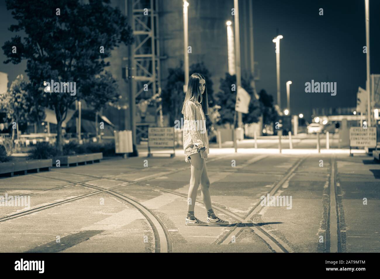 Gruselig monochromes Bild des trendigen Teenagers, der nachts durch die Gegend mit alten Bahngleisen mit industriellem Hintergrund spazieren geht. Stockfoto