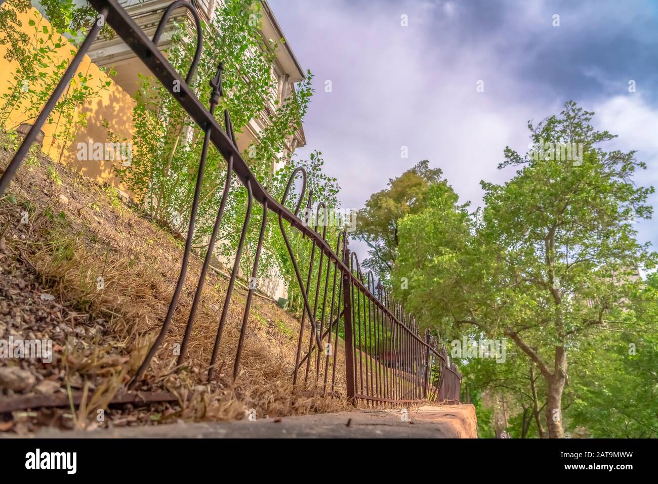 Beschädigter und rostiger Eisenzaun gegen weiße Baubäume und bewölkten Himmel Stockfoto