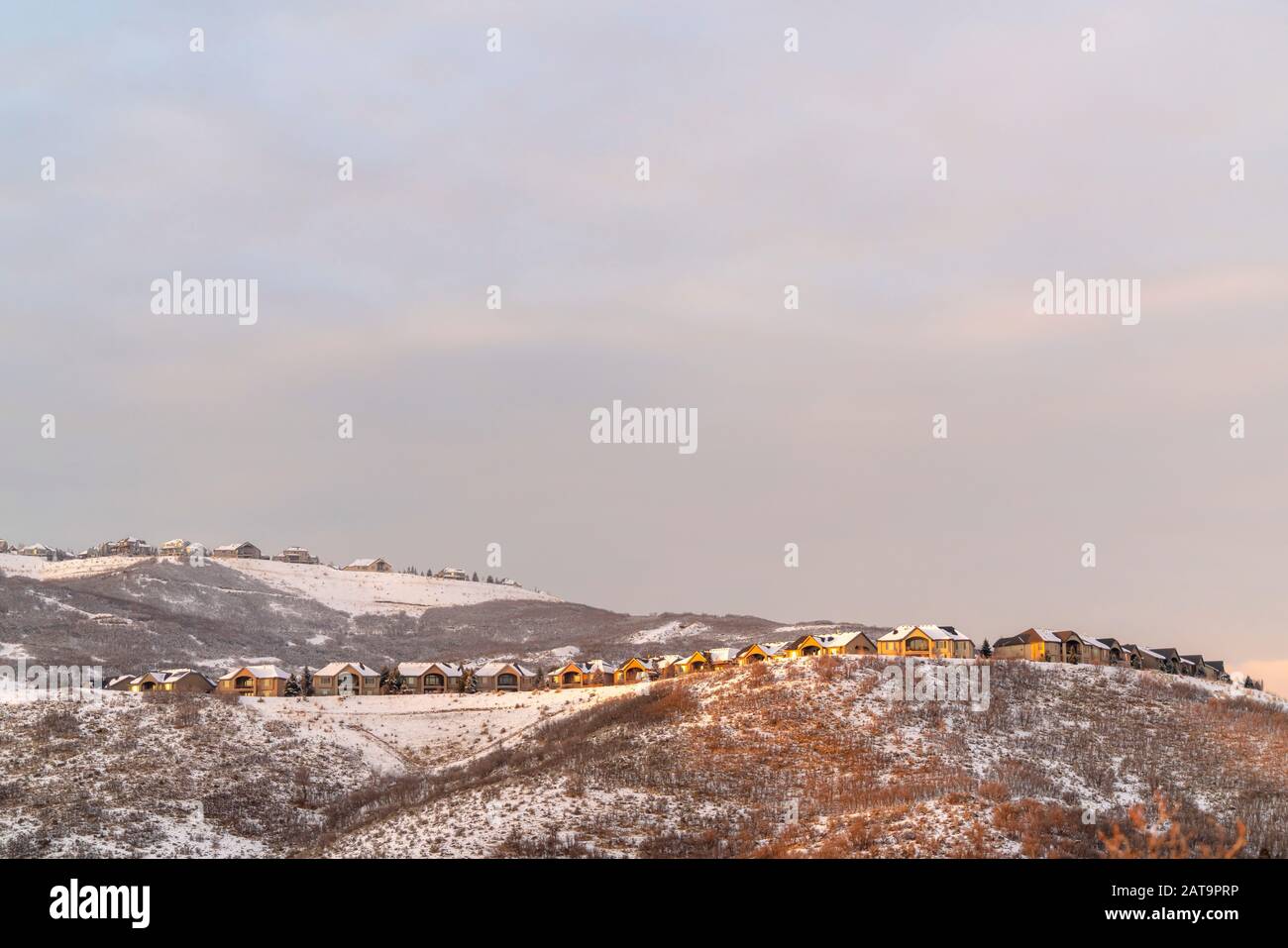 Häuser auf einem Hügel mit Panoramablick auf schneebedecktes Gelände und natürliche Schönheit bei Sonnenuntergang Stockfoto