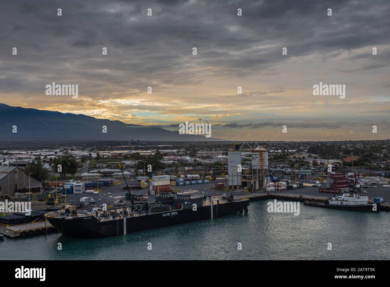 Kahului, Maui, Hawaii, USA. - 13. Januar 2020: Hilo Bay Doppelhüllen-Flüssigkeitstankbarge dockte im Hafen unter regnerischem, aber farbenfrohem Abendhimmel an. Gebäude Stockfoto