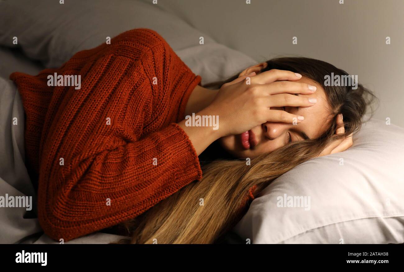 Junge Frau hat Schwierigkeiten einzuschlafen. Mädchen mit Schlaflosigkeit oder Kopfschmerzen bedecken ihr Gesicht mit der Hand. Stockfoto