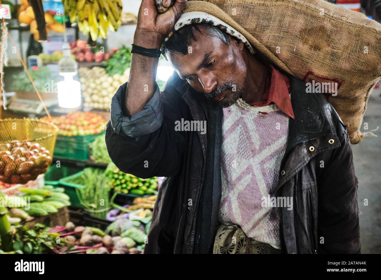 Ein Mann, der auf einem Markt in Sri Lanka große Tüten über Kopf und Schultern trägt Stockfoto