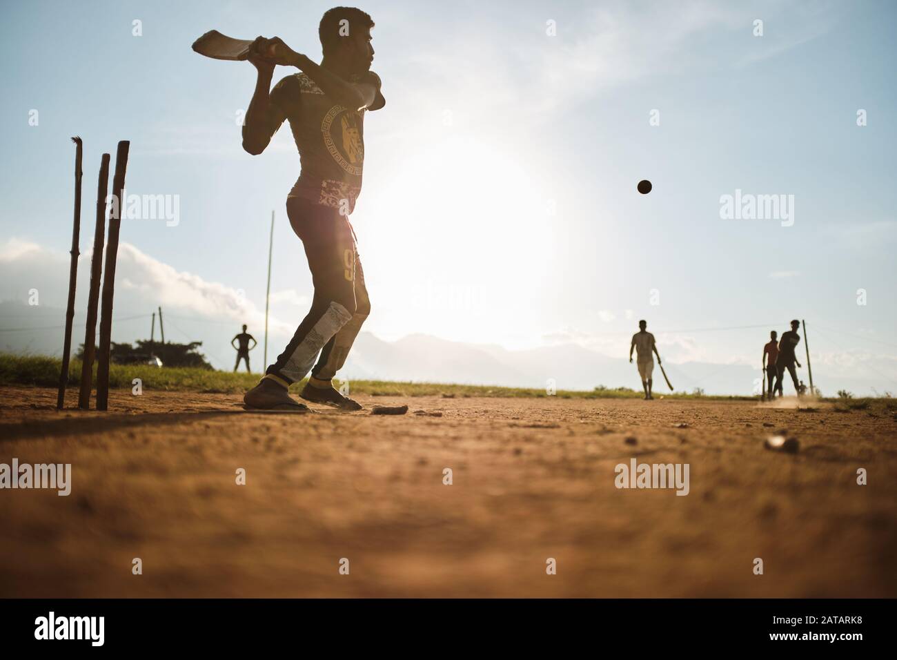 Jungen, die Cricket auf dem Feld in Sri Lanka mit Sonnenuntergang hinter ihnen spielen. Stockfoto