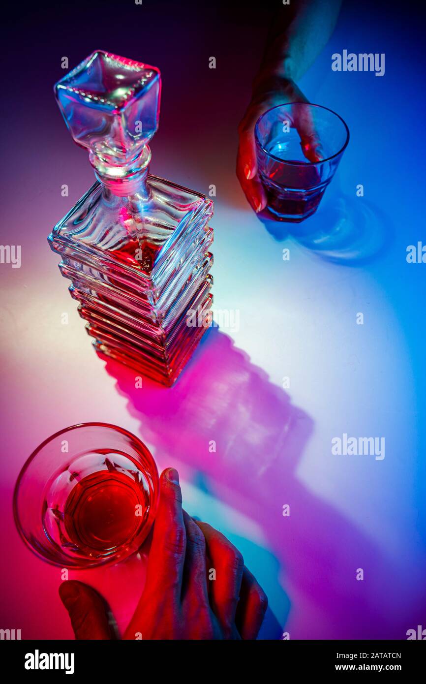 Glaskaraffe mit zwei Glasgläsern. Zwei Personen trinken von oben aus Alkohol Stockfoto