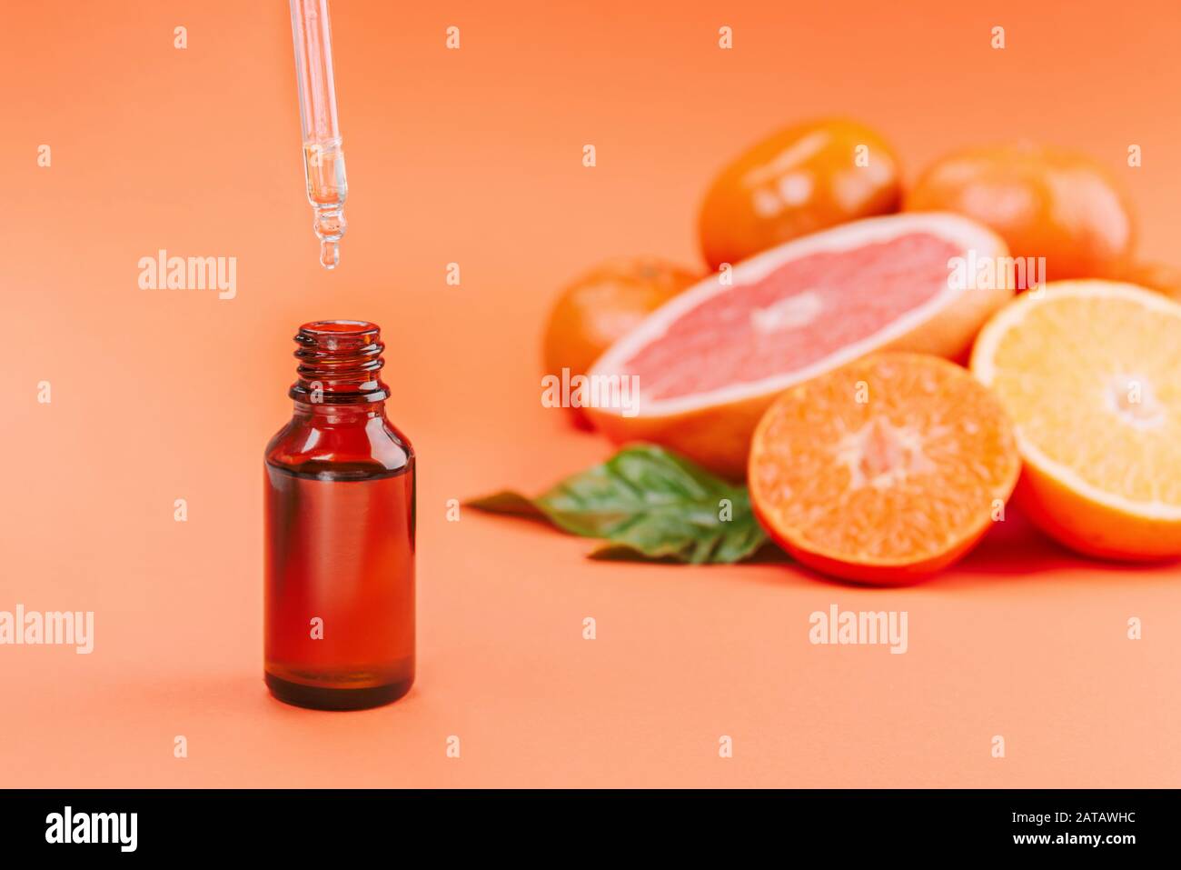 Frische reife Mandarinen, Grapefruit und Orangen mit grünen Blättern und Glasflasche mit ätherischem Öl auf orangefarbenem Hintergrund. Stockfoto