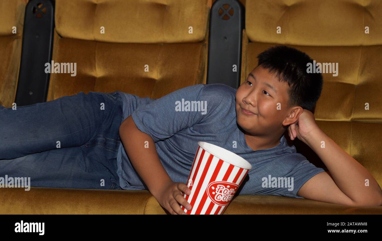 Der Junge legt sich Filme an und isst Popcorn glücklich und genießt im Kino. Stockfoto