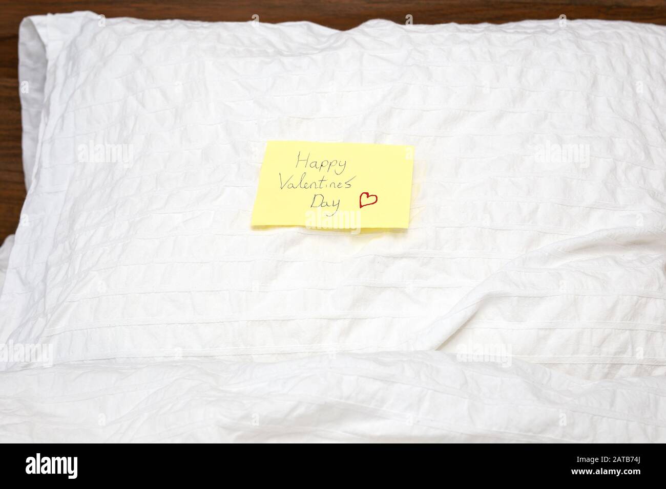 Abschluss einer gelben kleinen Notiz mit dem Text Happy Valentines Day darin geschrieben, auf dem Kissen weiße Bettlaken Stockfoto