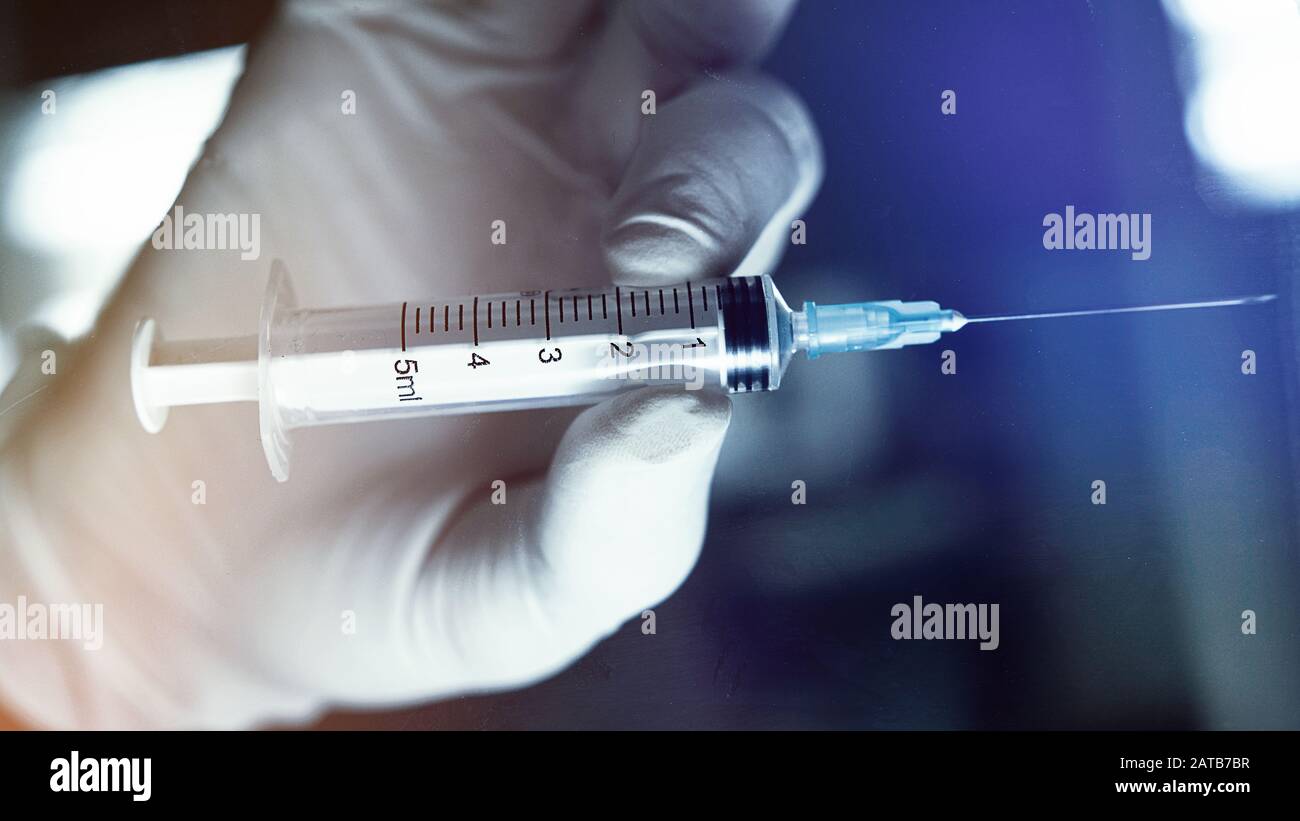 Ärzte oder medizinisches Personal, das eine Spritze in der Hand hält. Verschwommener Hintergrund mit Labormotiv. Stockfoto