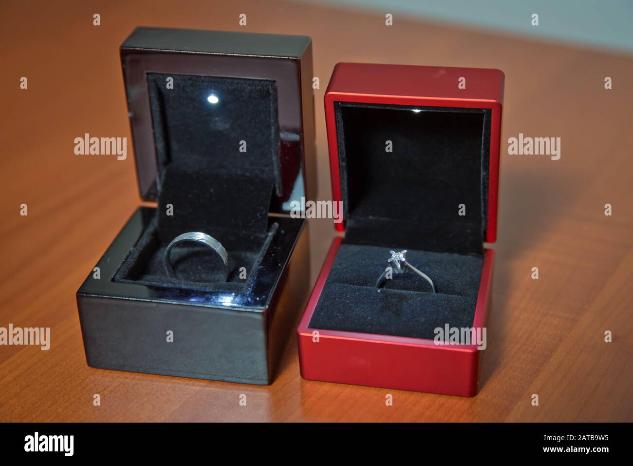 Paare Hochzeit Ringe in einem Geschenkkasten isoliert auf Holzhintergrund. Frau abd Mann Engagement Ringe . Hochzeit Ring in schwarz und rot Box woiden Stockfoto
