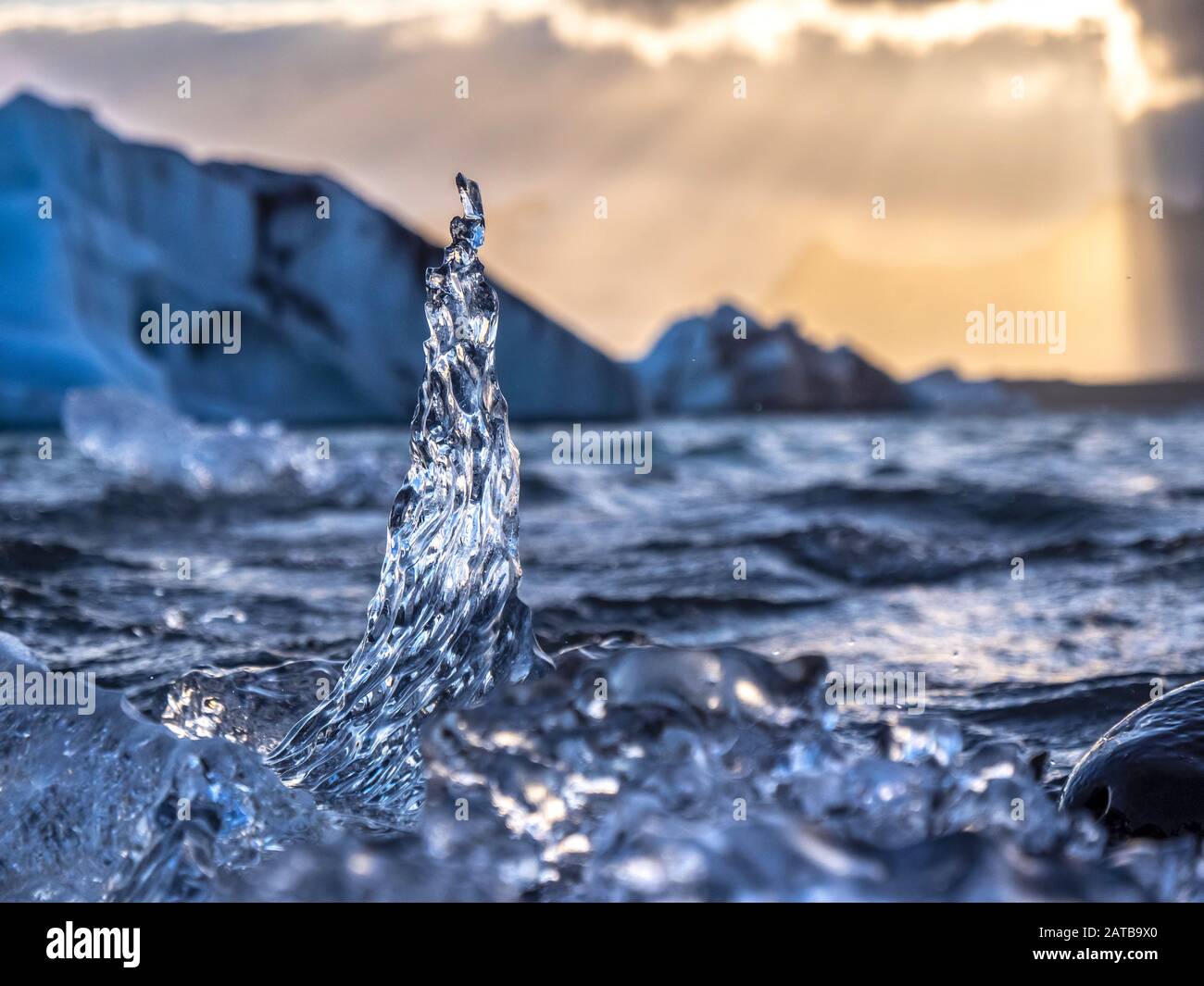 Ein Eiskristall ragt aus dem Wasser empor. Im Hintergrund bildet der versteckte Sonnenuntergang den perfecten Kontrast. Ein romantischer Moment. Stockfoto