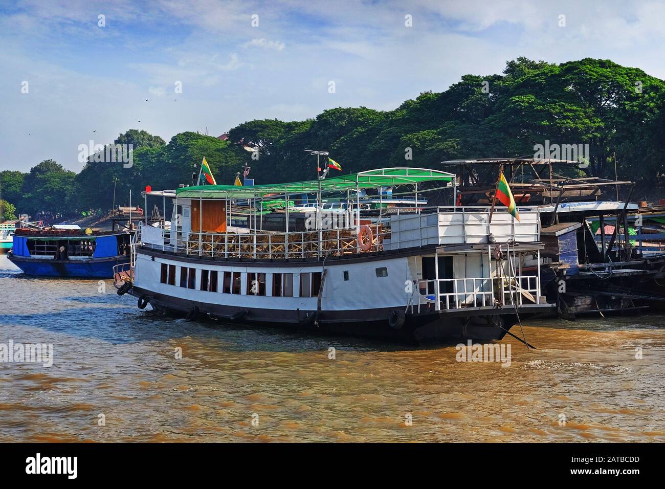 Traditionelle bunte birmanische Boote auf dem Fluss Irrawaddy, im Hafen von Mandalay, Myanmar, gegen grüne Vegetation und einen klaren blauen Himmel, der von bedeckt ist Stockfoto