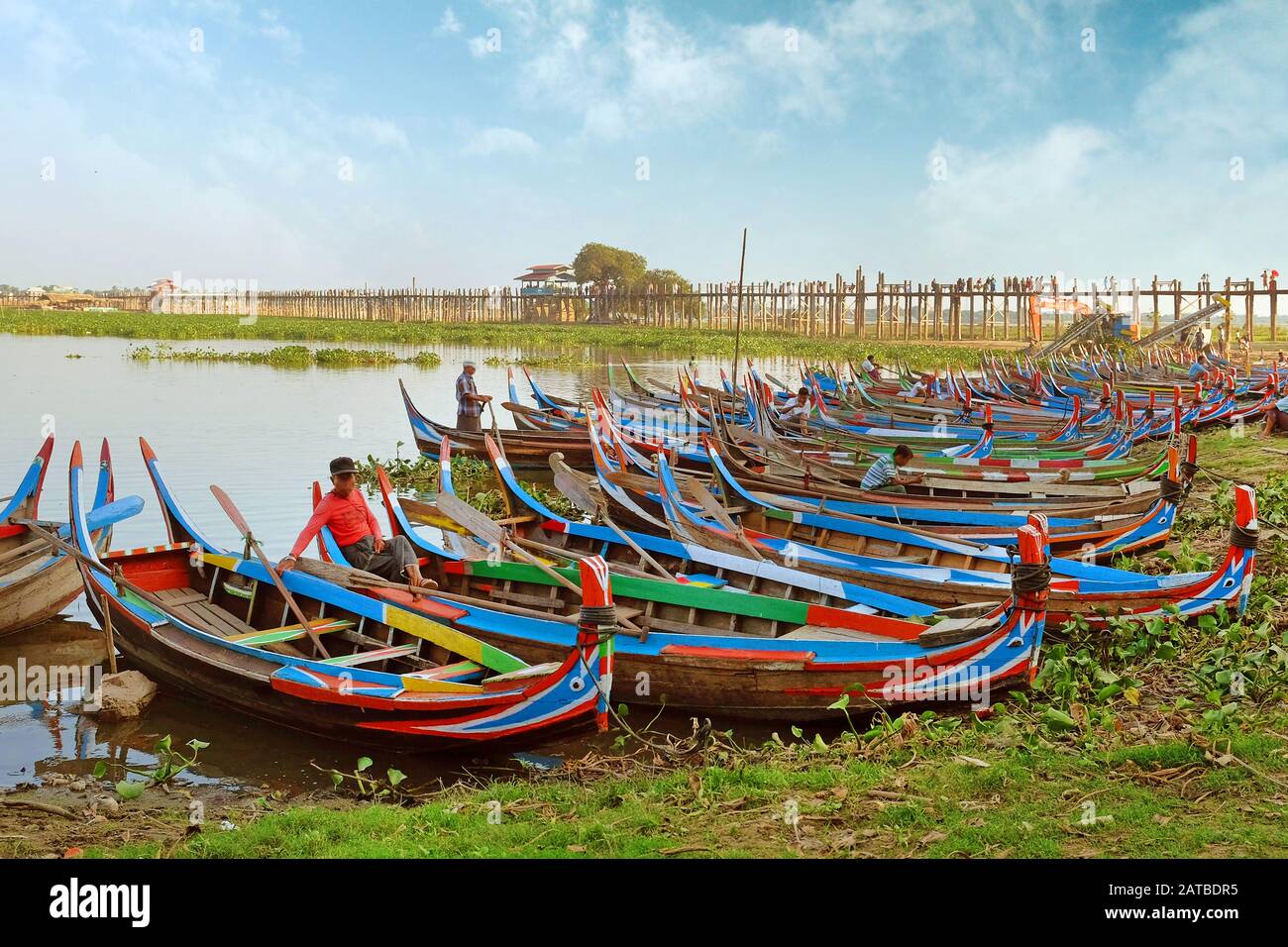 Bunte traditionelle Boote auf der Seite des Taung Tha Man Lake, in der Nähe von Mandalay, Myanmar, umgeben von grüner Vegetation, gegen einen klaren Himmel bedeckt Stockfoto