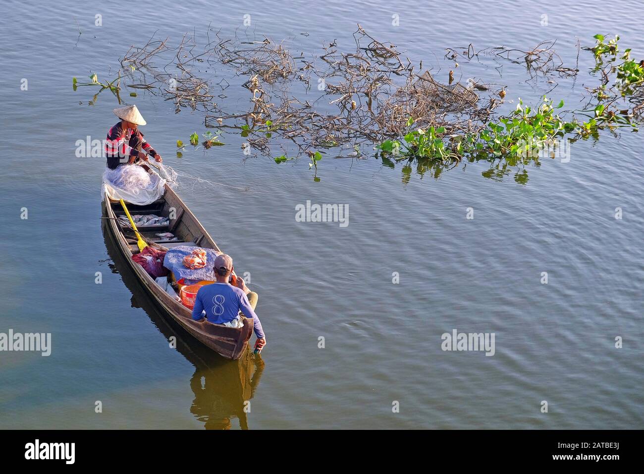 Menschen in einem traditionellen Fischerboot auf dem Taung Tha Man Lake, in der Nähe der U Bein-Brücke, Mandalay, in Myanmar, in der Nähe schwimmender grüner Vegetation. Stockfoto