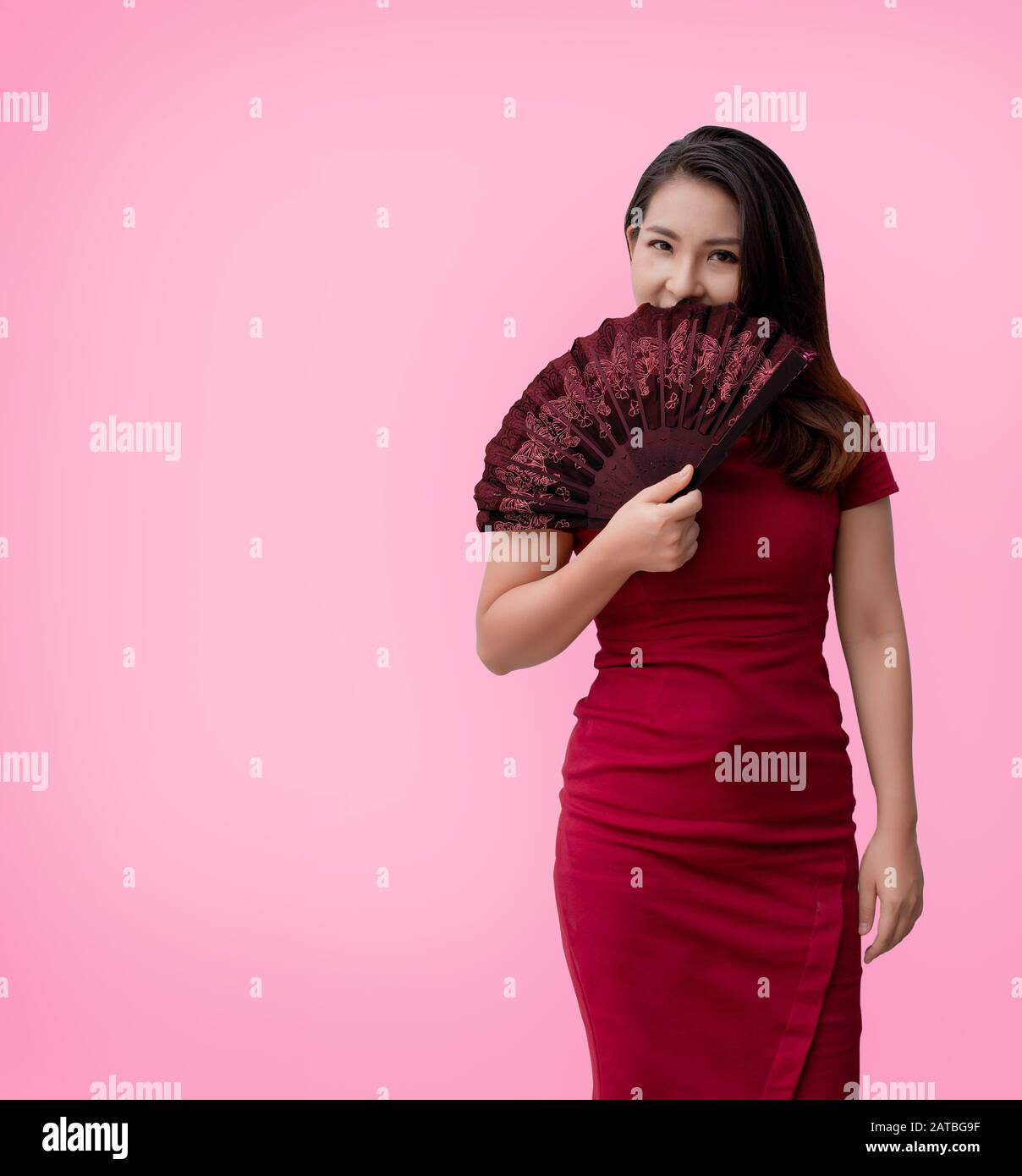 Selbstbewusste chinesin aus asien mit Papierlüfter in rotem Kleid auf rotem Hintergrund (Inklusive Beschneidungspfad) Stockfoto