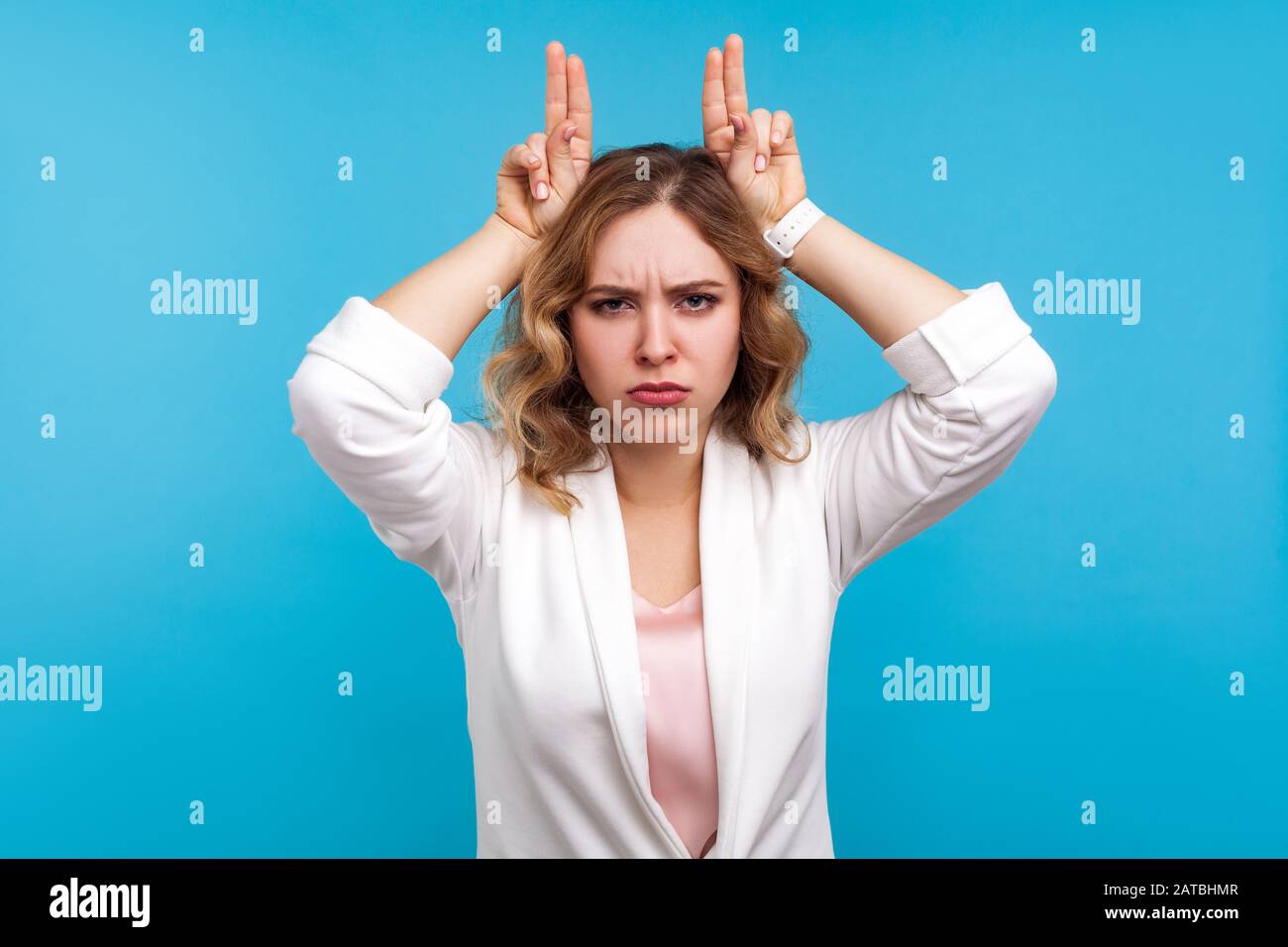 Portrait einer aggressiven Frau mit gewelltem Haar in weißer Jacke, die Stierhörner über ihren Kopf und ihr frommendes Gesicht Geste, was die Gefahr von Wut zum Ausdruck bringt. Stockfoto