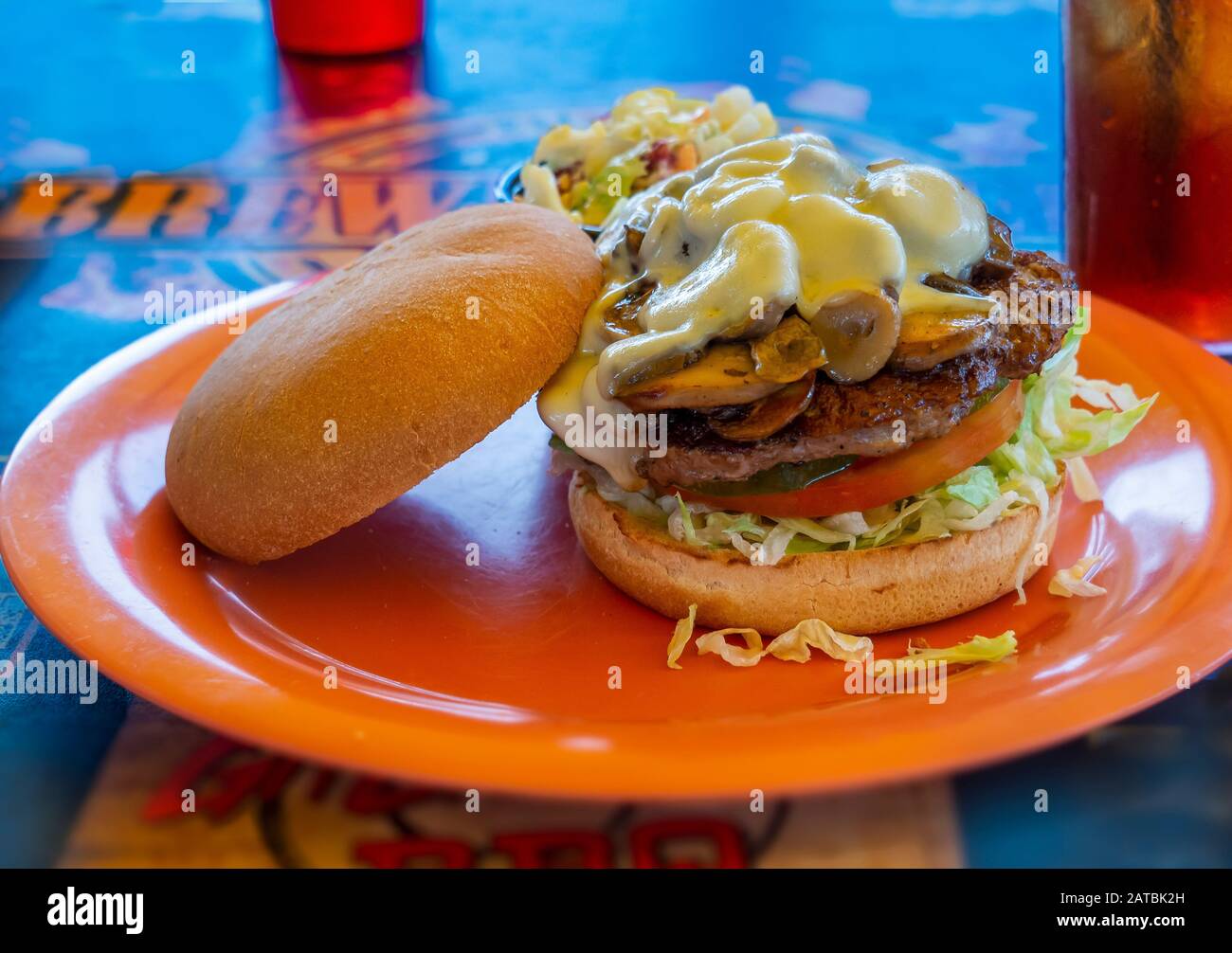 Hamburger Sandwich mit Bun, Pilzen, Käse, Salat und Tomaten auf orangefarbenem Teller mit blauem Hintergrund Stockfoto