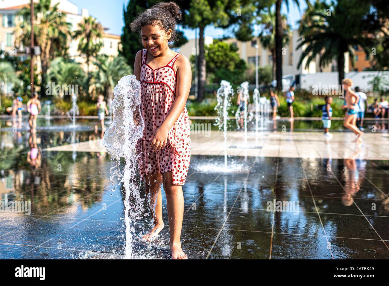 Das Kind hat Spaß mit einem Wasserstrahl, der sich im Mirroir d'eau am neuen städtischen Ort, der Promenade du Paillon in Nizza, Frankreich, befindet Stockfoto