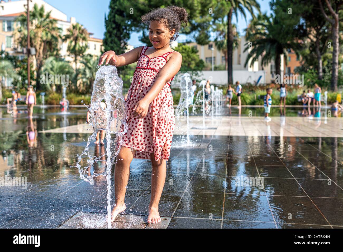 Das Kind hat Spaß mit einem Wasserstrahl, der sich im Mirroir d'eau am neuen städtischen Ort, der Promenade du Paillon in Nizza, Frankreich, befindet Stockfoto