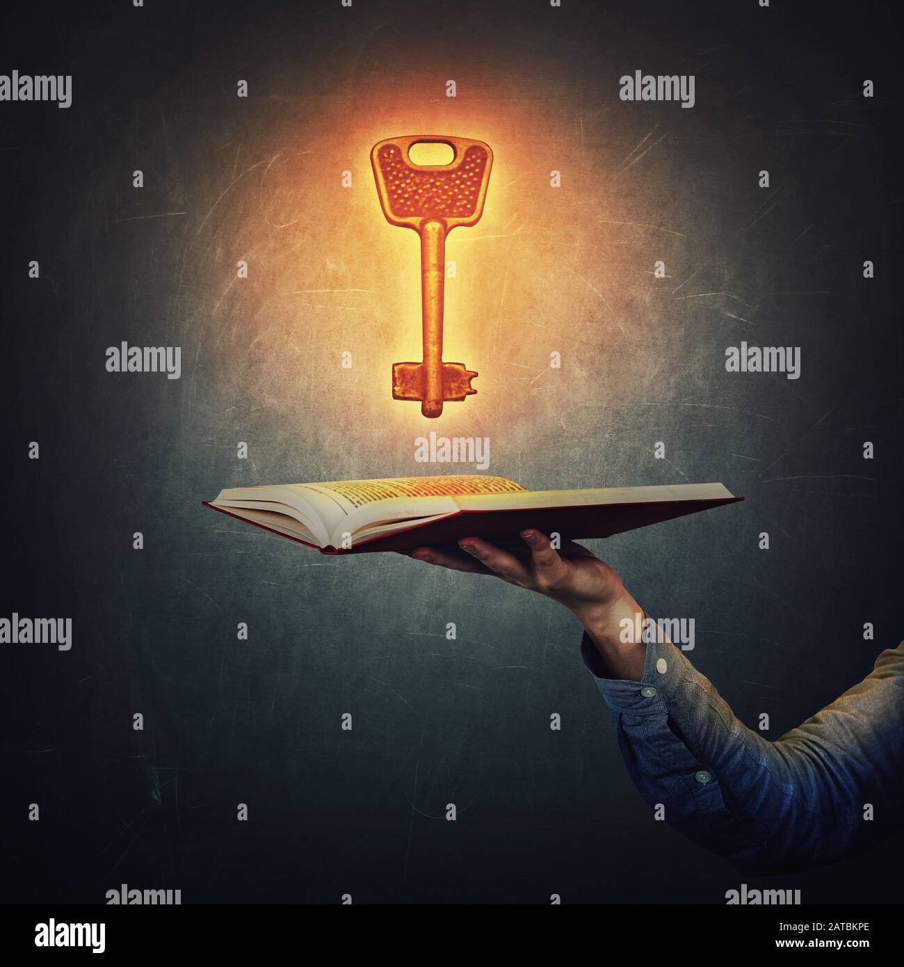 Hand der männlichen Studenten, die ein offenes Buch mit einem magisch glänzenden, goldenen Schlüssel über einem dunklen Hintergrund auf der Tafel hält. Symbol für unbegrenzten Zugriff auf Wissen und Stockfoto