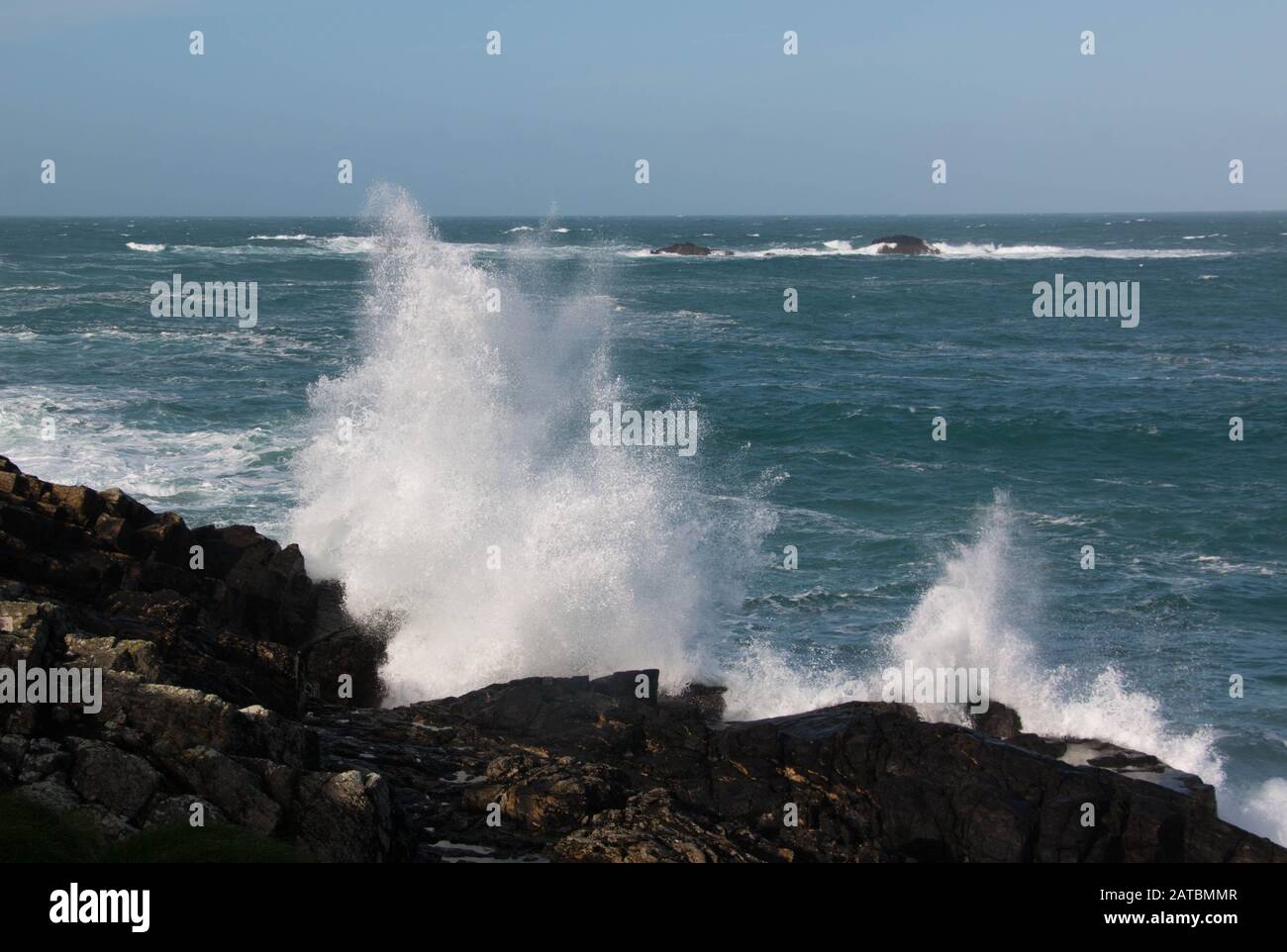 Wellen, die auf Felsen mit blauem Himmel in Pendeen, Cornwall abstürzen Stockfoto