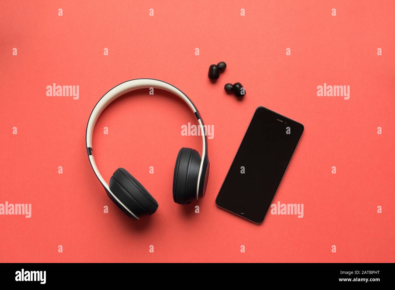 Fotos von großen und kleinen bluetooth-kopfhörern und einem Smartphone zur Wiedergabe von Musik auf rotem Hintergrund Stockfoto