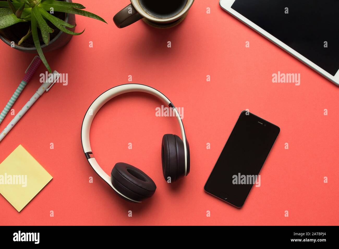 Fotos von Bluetooth-Kopfhörern und Smartphone vorrätig, um Musik auf rotem Hintergrund zu hören. Einige Desktop-Objekte um sie herum Stockfoto