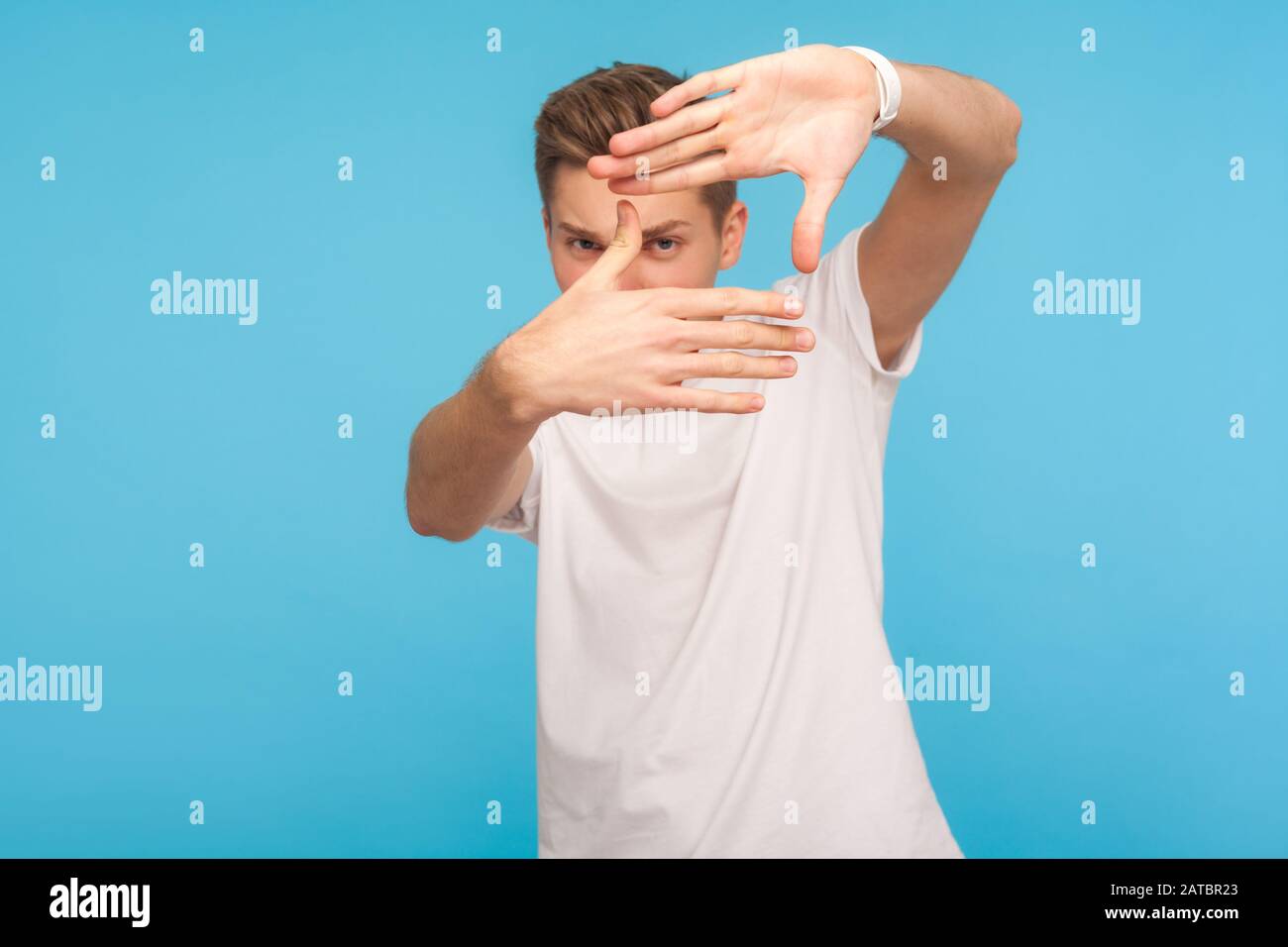 Porträt eines neugierigen Mannes in weißem T-Shirt Gesting Bilderrahmen mit Händen, Blick durch die Finger und Fokussierung auf interessanten Moment, Foto machen. Stockfoto