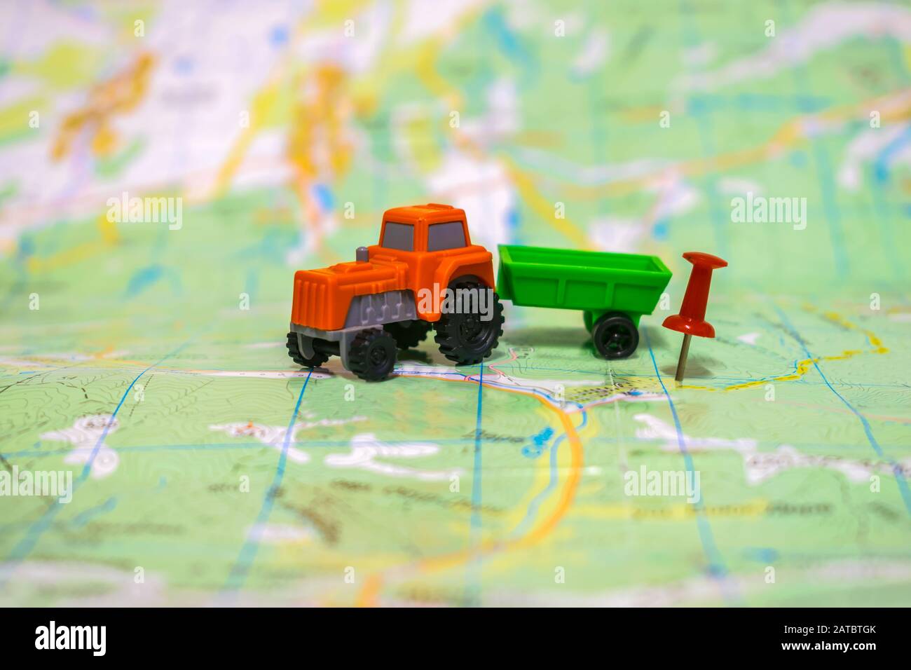 Der orangefarbene Traktor bewegt sich zum Hof. Ein Spielzeugschlepper befindet sich auf einer Karte. Das Konzept der Landwirtschaft. Stockfoto
