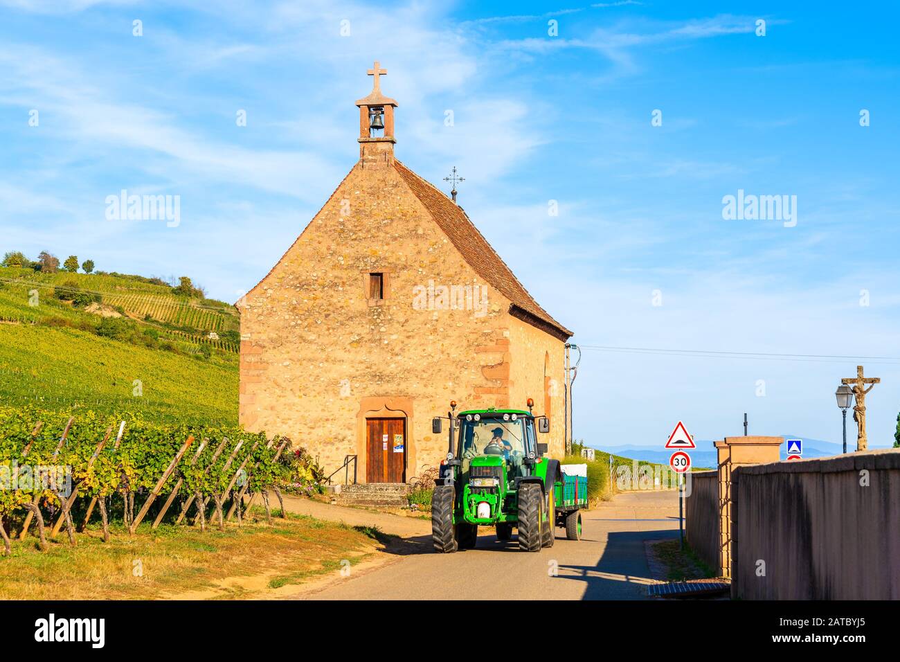 Alsace, FRANKREICH - SEP 20, 2019: Traktor fährt auf der Straße in der Nähe von Weinbergen des Dorfes Kientzheim mit alter Kirche im Hintergrund, Elsaß Weinstraße, Frankreich. Stockfoto