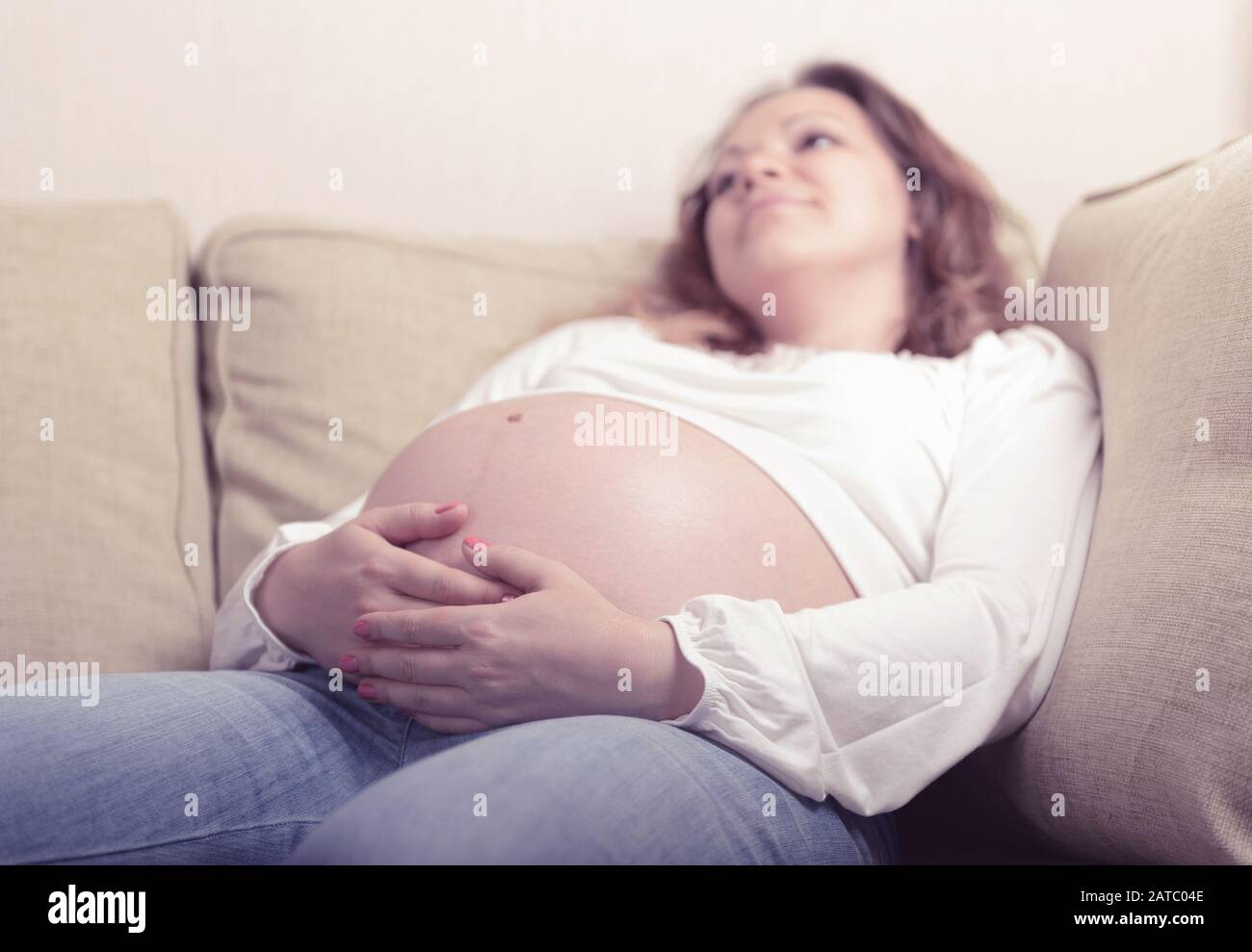 Pensive schwangere Frau sitzt zu Hause auf dem Sofa. Der neunte Schwangerschaftsmonat. Stockfoto