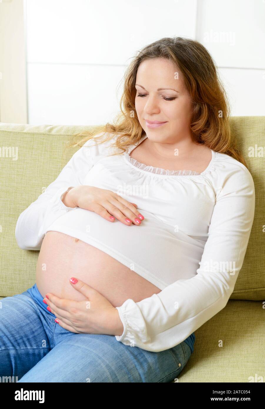 Glückliche schwangere Frau, die zu Hause auf der Couch sitzt. Der neunte Schwangerschaftsmonat. Stockfoto