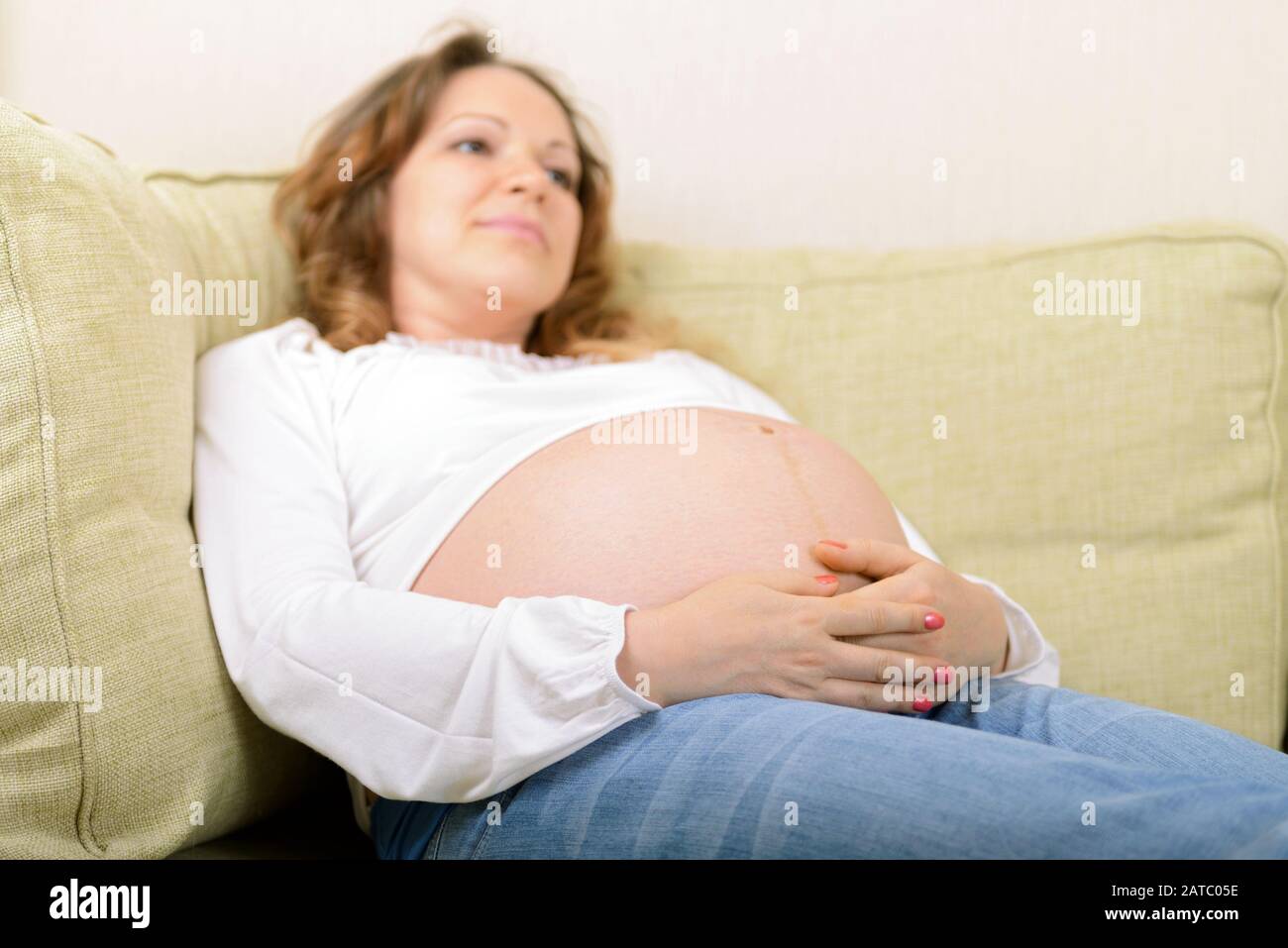 Pensive schwangere Frau sitzt zu Hause auf dem Sofa. Der neunte Schwangerschaftsmonat. Stockfoto