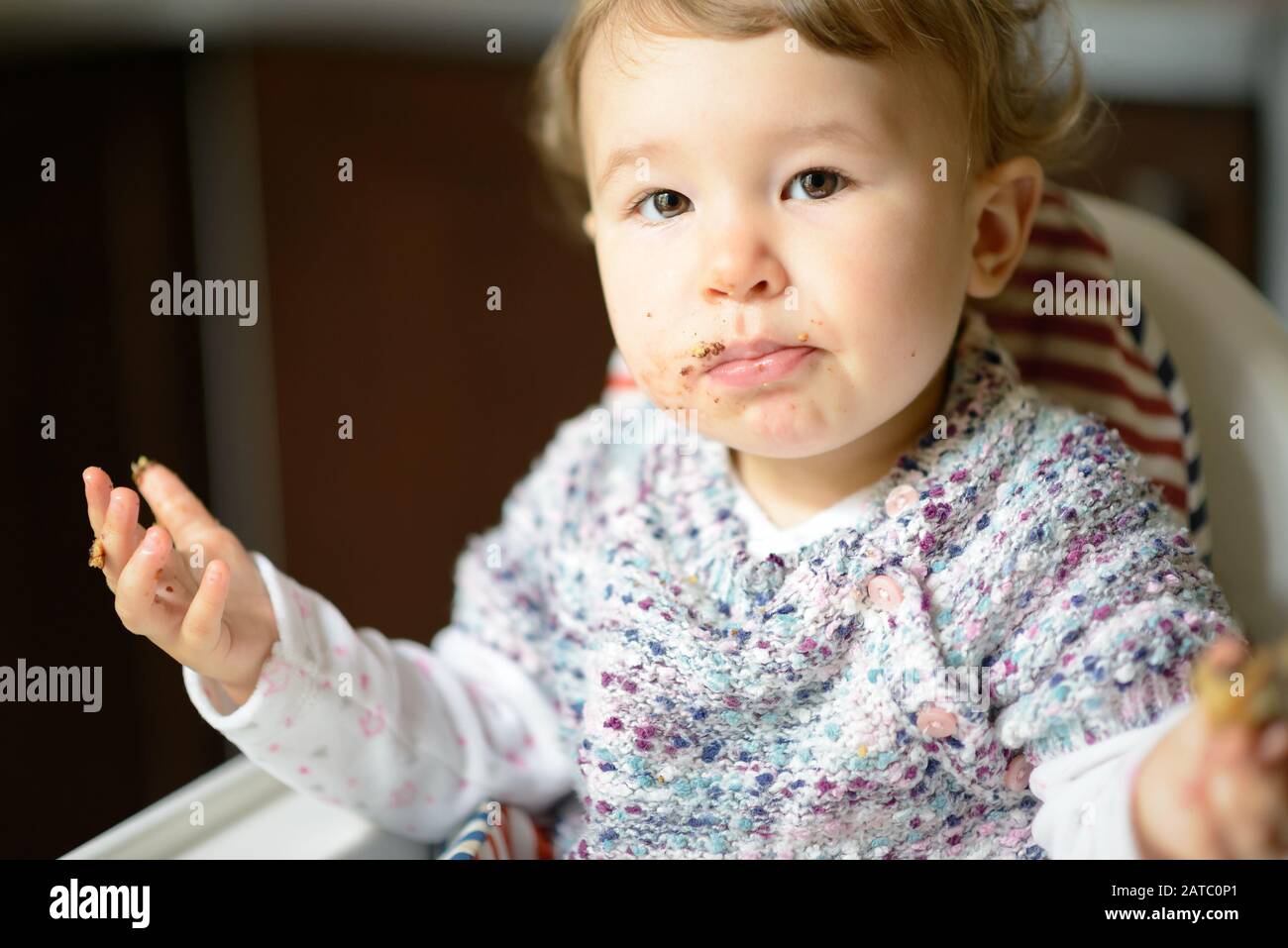 Baby Mädchen mit unordentlichen Gesichtern essen. Das nette einjährige Kind isst und schaut sich die Kamera an. Stockfoto