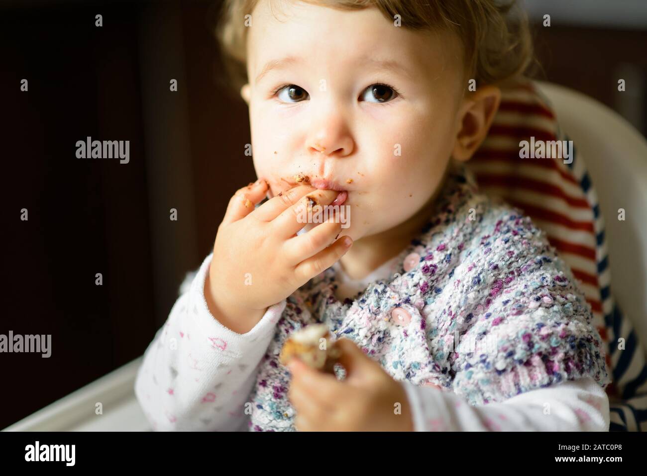 Baby Mädchen mit unordentlichen Gesichtern essen. Das einjährige Kind isst und steckt sich die Finger in den Mund. Stockfoto