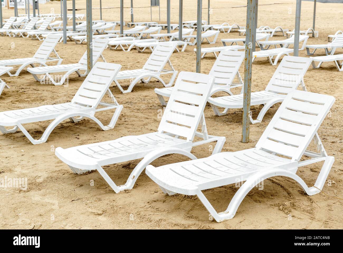 Liegen in der Saison. Viele leerstehende Sonnenliegen an einem sandigen Strand. Panorama von vielen weißen Sonnenliegen aus Kunststoff am Meeresufer. Desertierte Ferienanlage bea Stockfoto